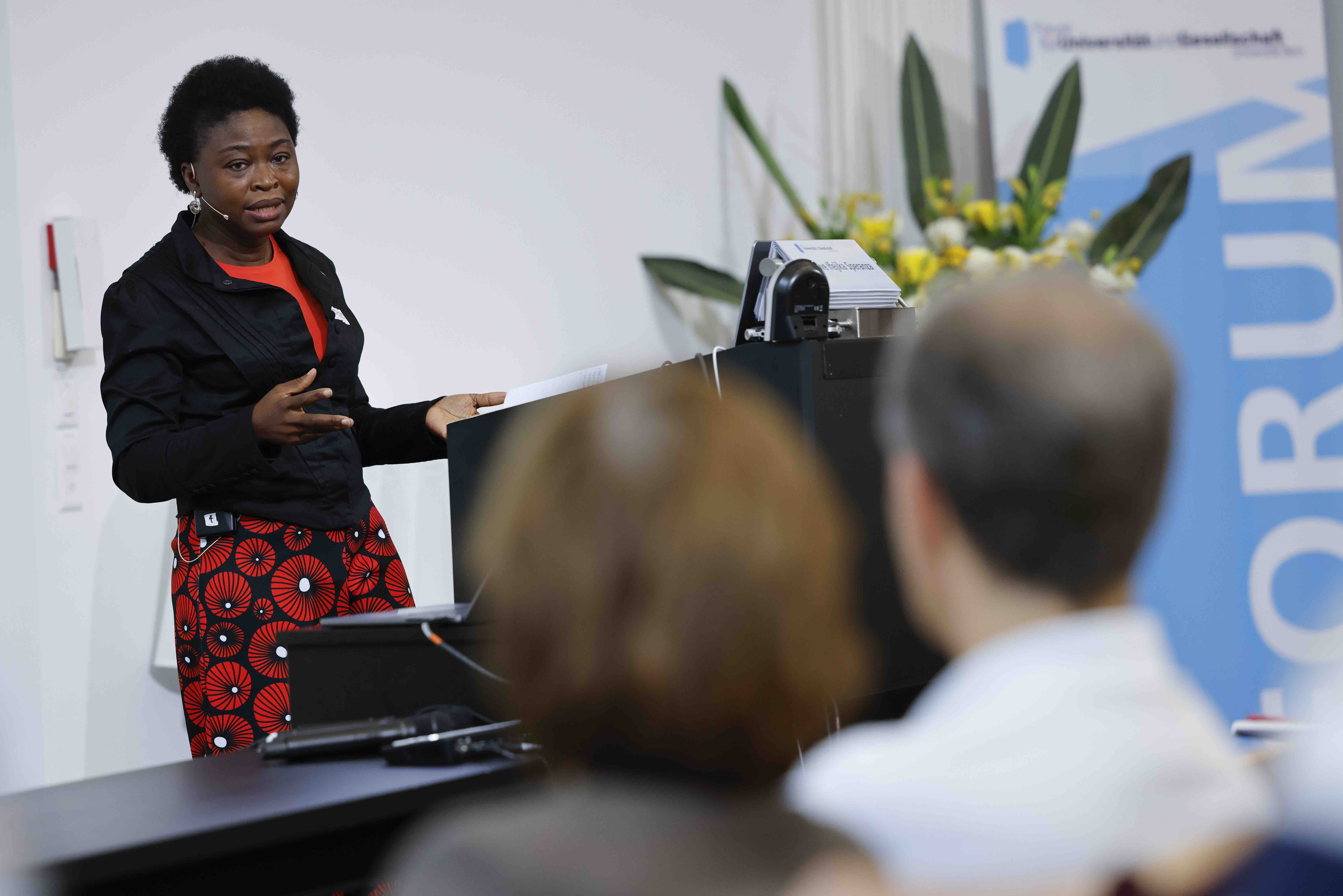 Geographieprofessorin Chinwe Ifejika Speranza während ihrem Referat. Sie steht hinter einem Rednerpult, im Vordergrund sind Zuhörer:innen sichtbar.