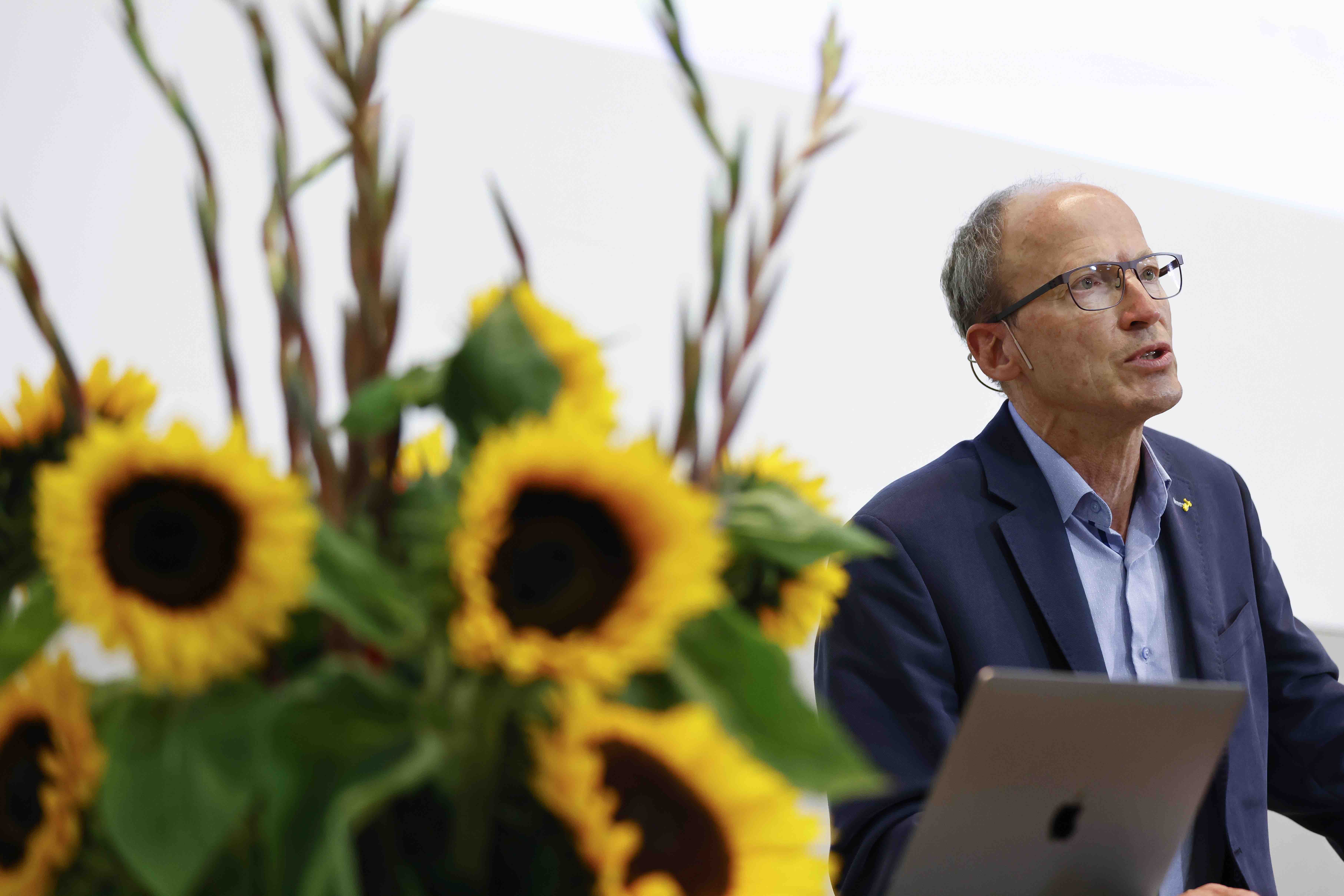 Dr. Matthias Kamber während seinem Referat zum Thema Doping. Im Vordergrund des Bildes steht ein grosser Strauss mit Sonnenblumen.