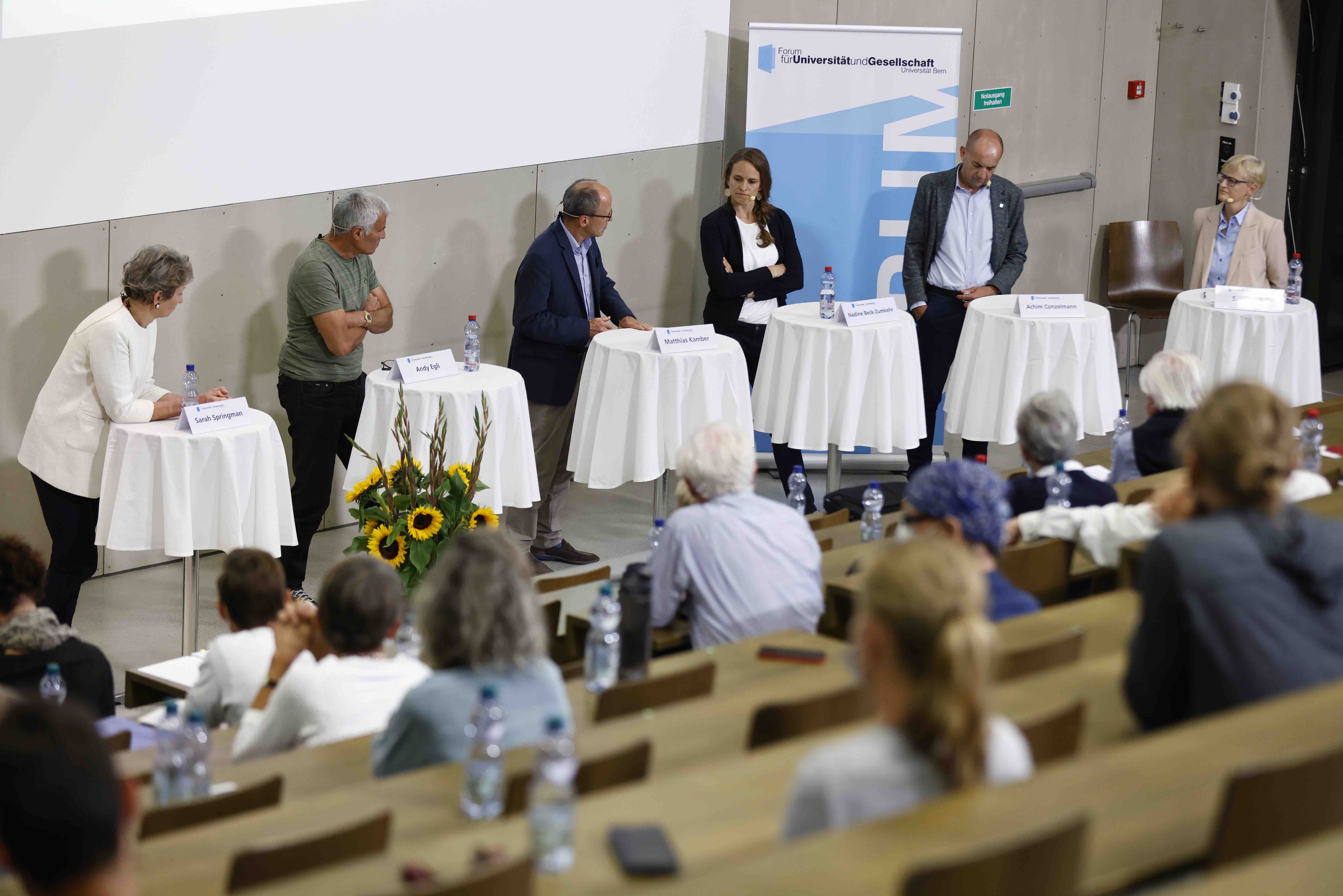 Sarah Springman, Andy Egli, Matthias Kamber, Nadine Beck und Achim Conzelmann diskutieren mit der Moderatorin Susy Schär. Sie stehen an Stehtischen mit weissen Tischtüchern, im Vordergrund ist ein Teil des Publikums sichtbar.