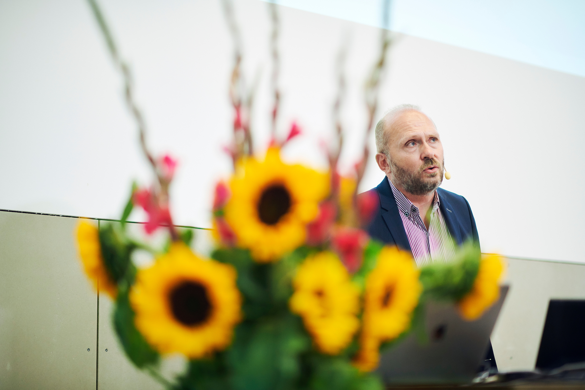 Der Referent Claudio Nigg vom Institut für Sportwissenschaft während seinem Vortrag an der Universität Bern. Neben ihm steht ein Strauss Sonnenblumen als Raumschmuck.