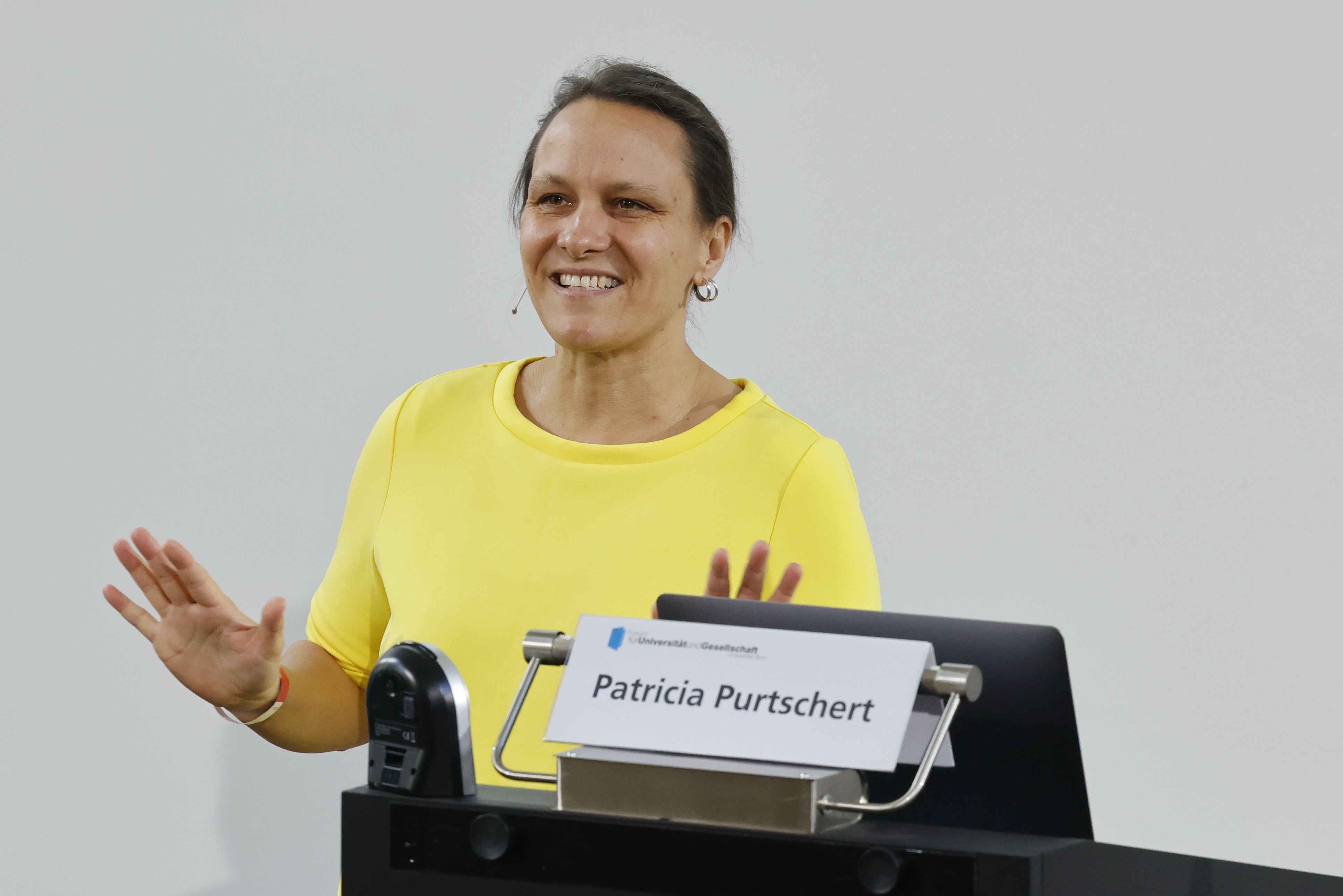 Die Referentin Prof. Dr. Patricia Purtschert vom Interdisziplinären Zentrum für Geschlechterforschung der Universität Bern während ihrem Referat. Sie steht hinter einem Rednerpult mit einem Laptop und gestikuliert mit den Händen.