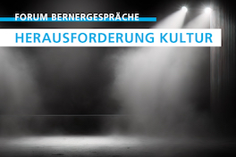 Schwarz-Weiss-Foto einer leeren Bühne mit einem Lichtkegel von drei Scheinwerfern; in den Lichtstrahlen ist feiner Nebel sichtbar.