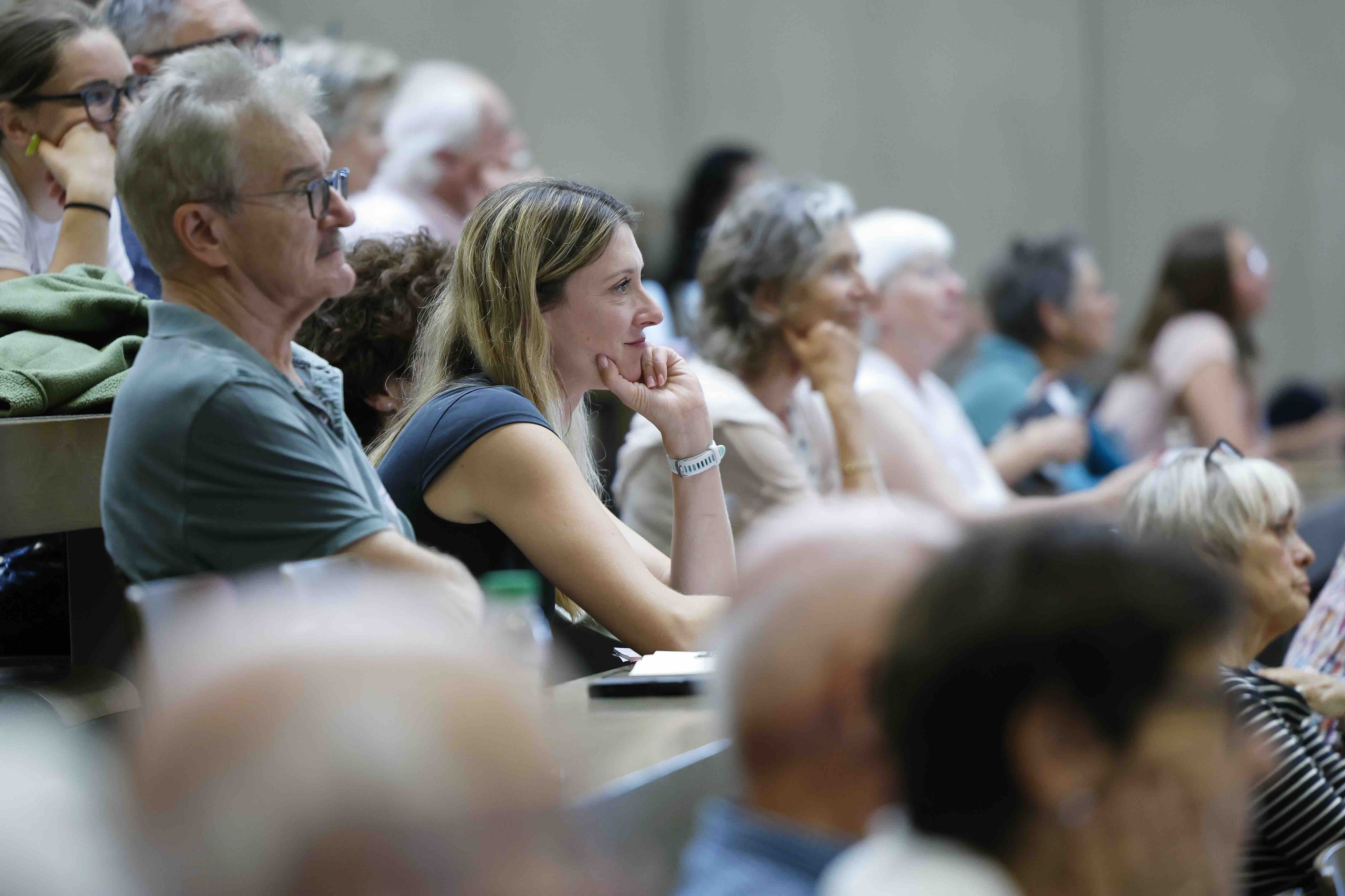 Menschen unterschiedlichen Alters sitzen aufmerksam in einem Hörsaal und hören einem Vortrag zu.