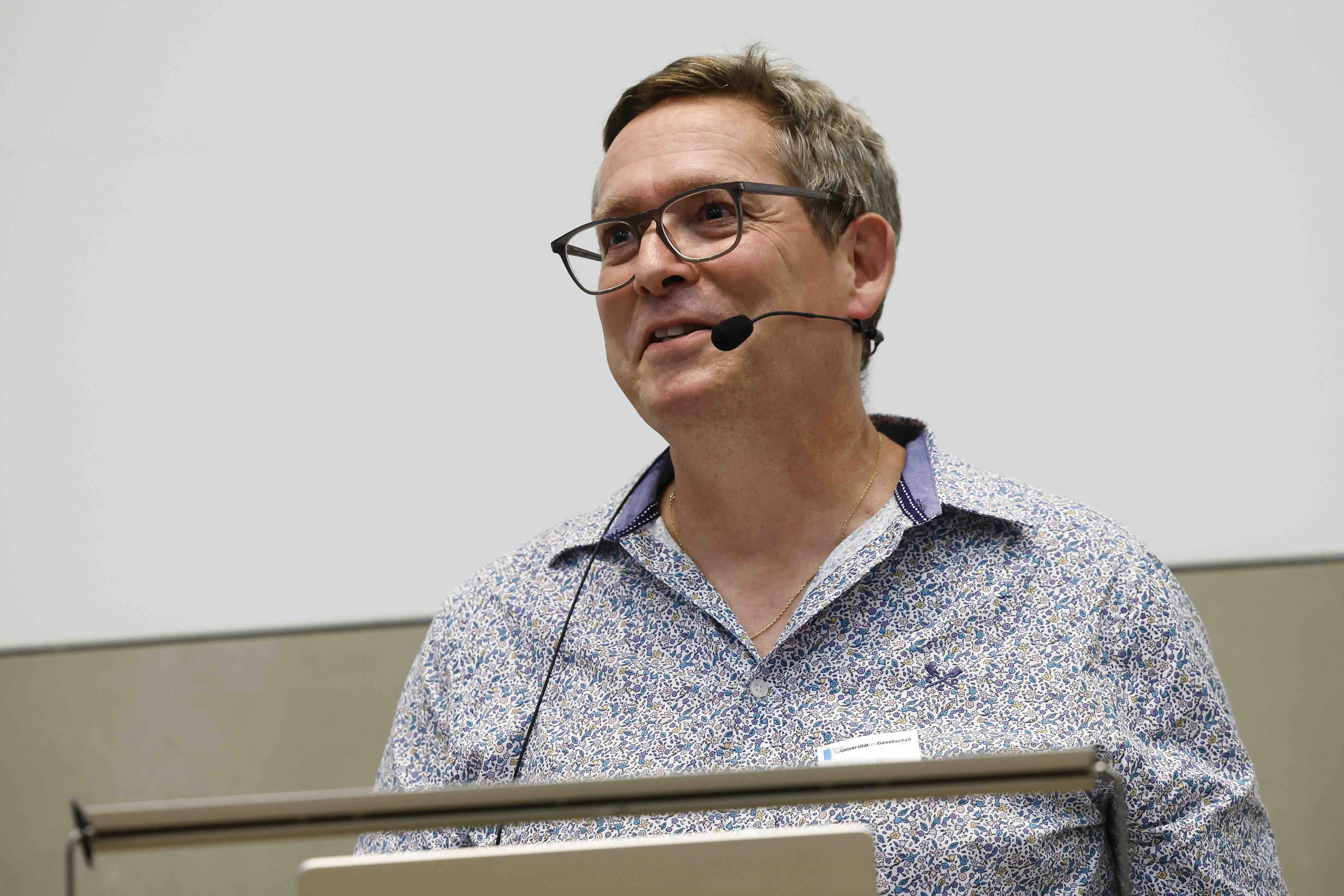 Oliver Hämmig hält mit Mikrofon ein Referat zur Einsamkeit und blickt zum Publikum.