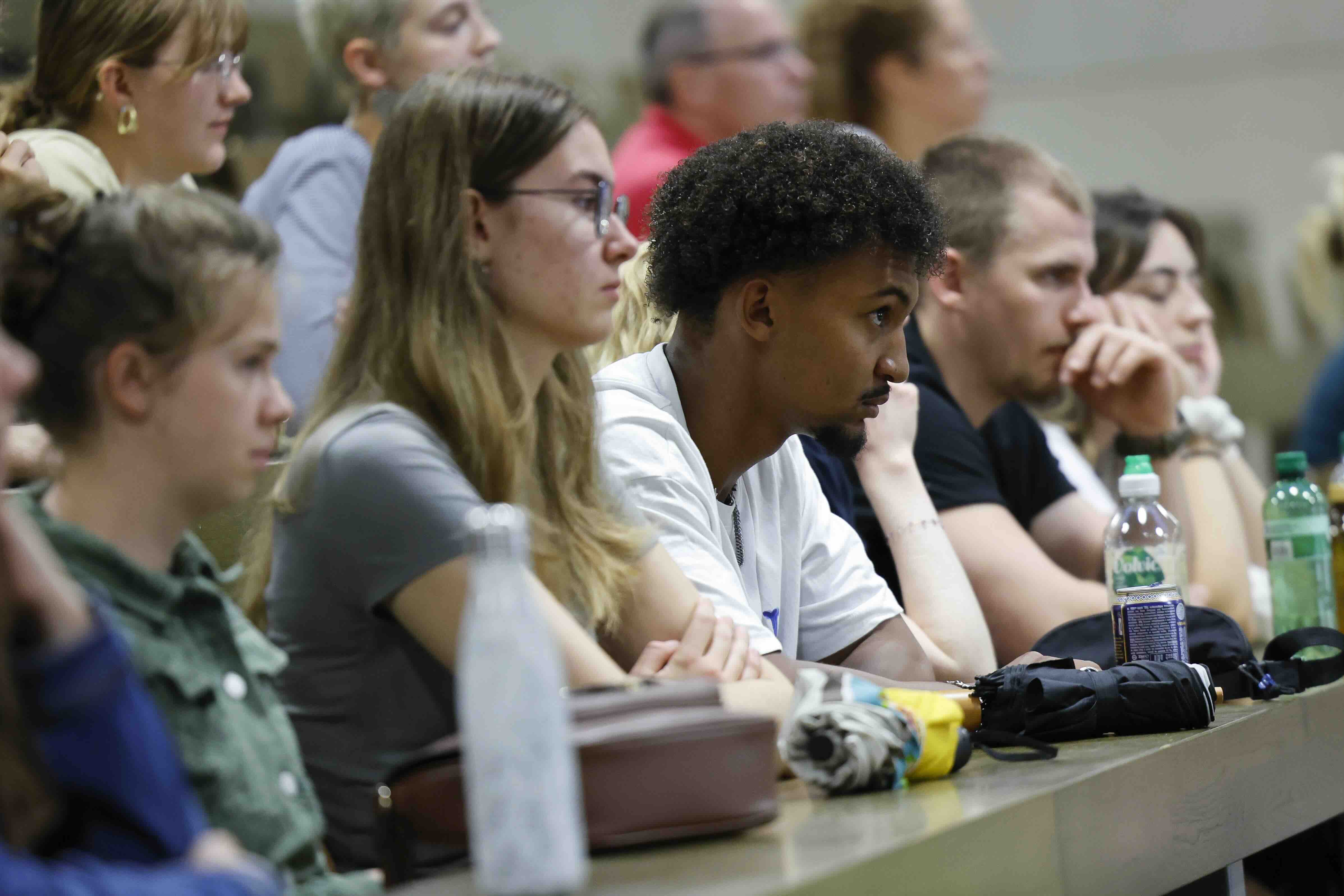 Mehrere junge Erwachsene sitzen im Hörsaal und verfolgen konzentriert einen Vortrag.