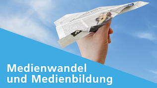 Eine Hand hält einen Papierflieger aus Zeitungspapier, kurz vor dem Loslassen, vor blauem Hintergrund.