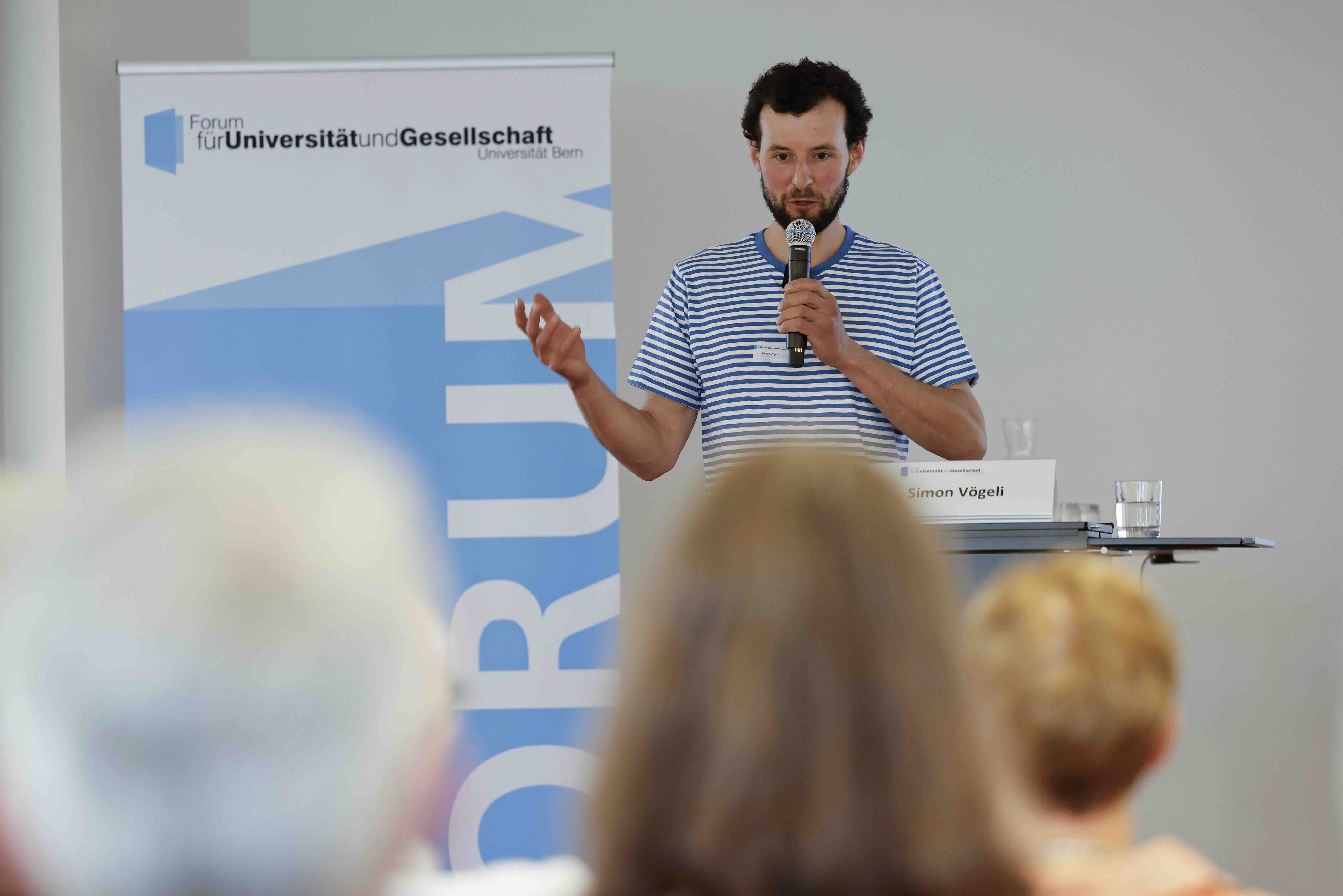 Der Referent Simon Vögeli steht vor dem Publikum uns spricht darüber, wie er seinen Biohof Stauffenbühl klimaneutral führen will.