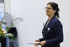 Die Moderatorin Lisa Stalder trägt einen dunkelblauen Blazer. Sie hat dunkle Haare und trägt eine Brille mit dunklem Gestell.
