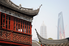 Häuser mit Pagodendächern stehen im Vordergrund, im Hintergrund sind Hochhäuser und Baukräne zu sehen.