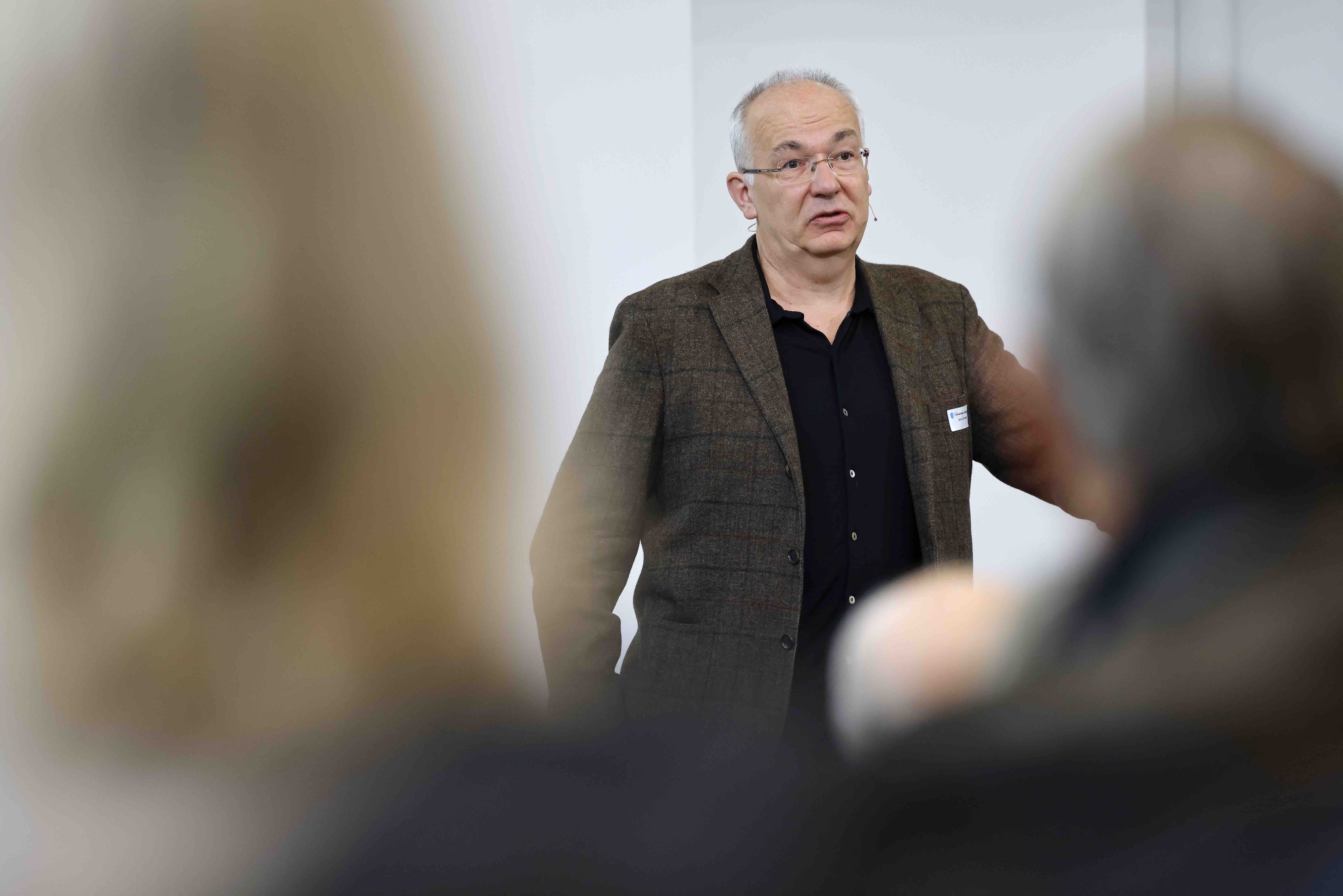 Aufnahme des Referenten Jens Schlieter, der in einem dunklen Anzug vor dem Publikum steht.