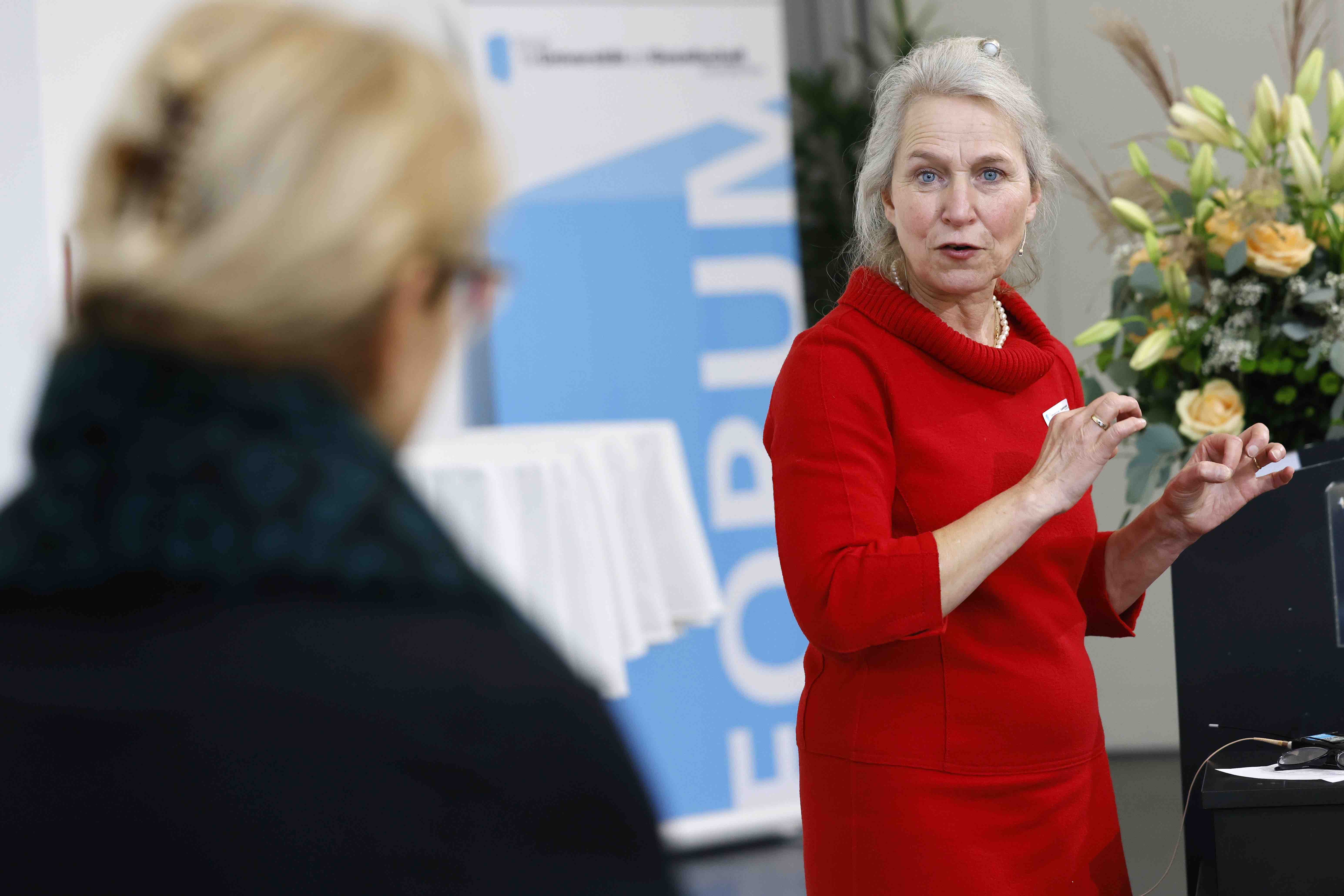 Die Moderatorin Ursula Hürzeler von hinten im Gespräch mit der Referentin Christine Brombach, die ein rotes Kleid trägt und am gestikulieren ist.