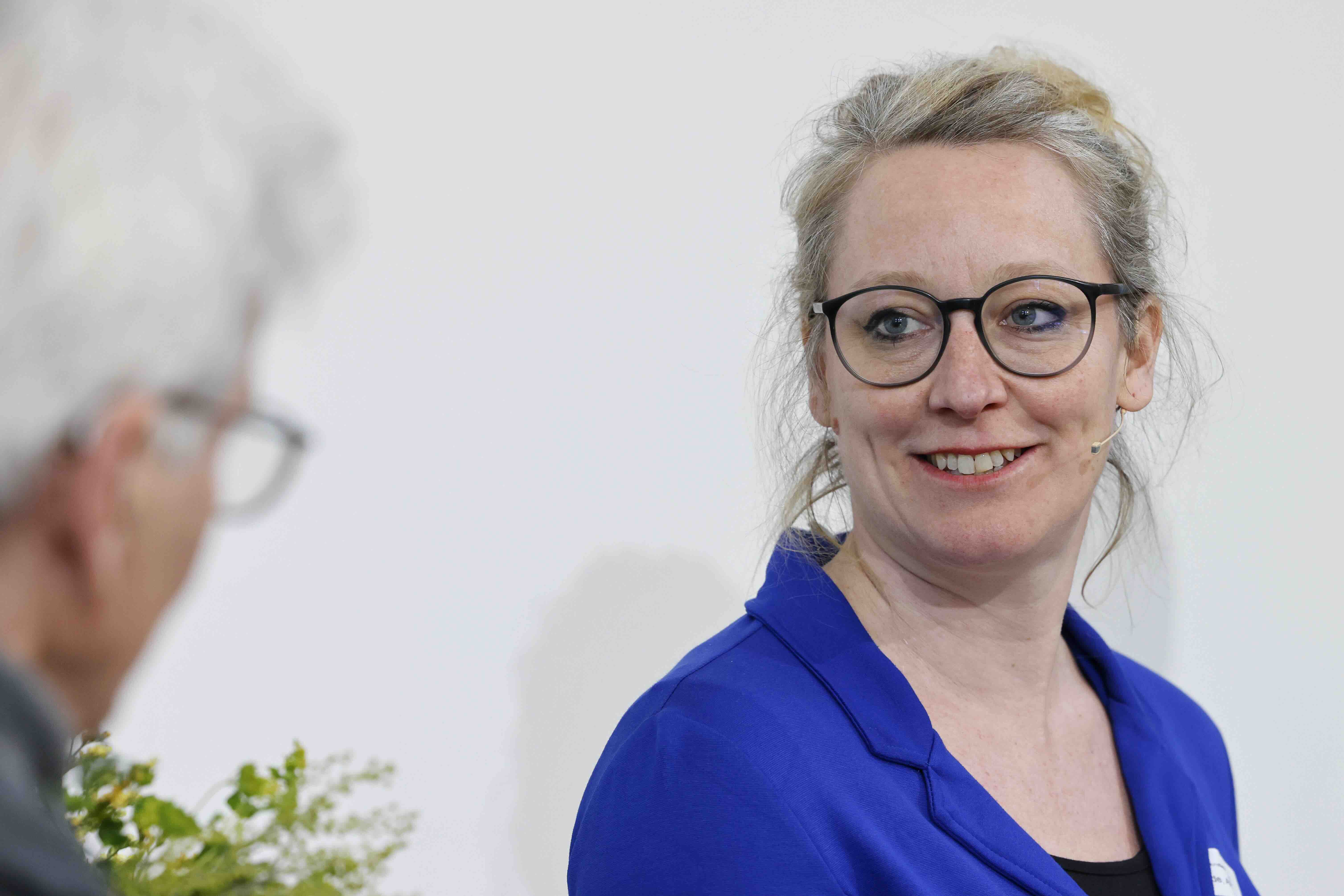 Eine Frau in violettem Kleid und mit Brille blickt zum Moderator, mit dem sie im Gespräch ist.
