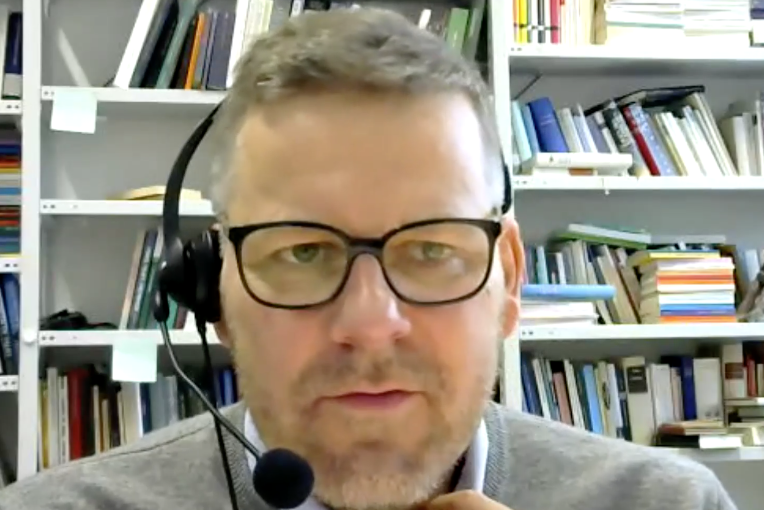 Ein Porträt von Prof. Dr. Martin Hartmann während seinem Online-Vortrag zum Thema «Misstrauen und Vertrauen in historischer Perspektive». Im Hintergrund ist ein Büchergestell sichtbar.