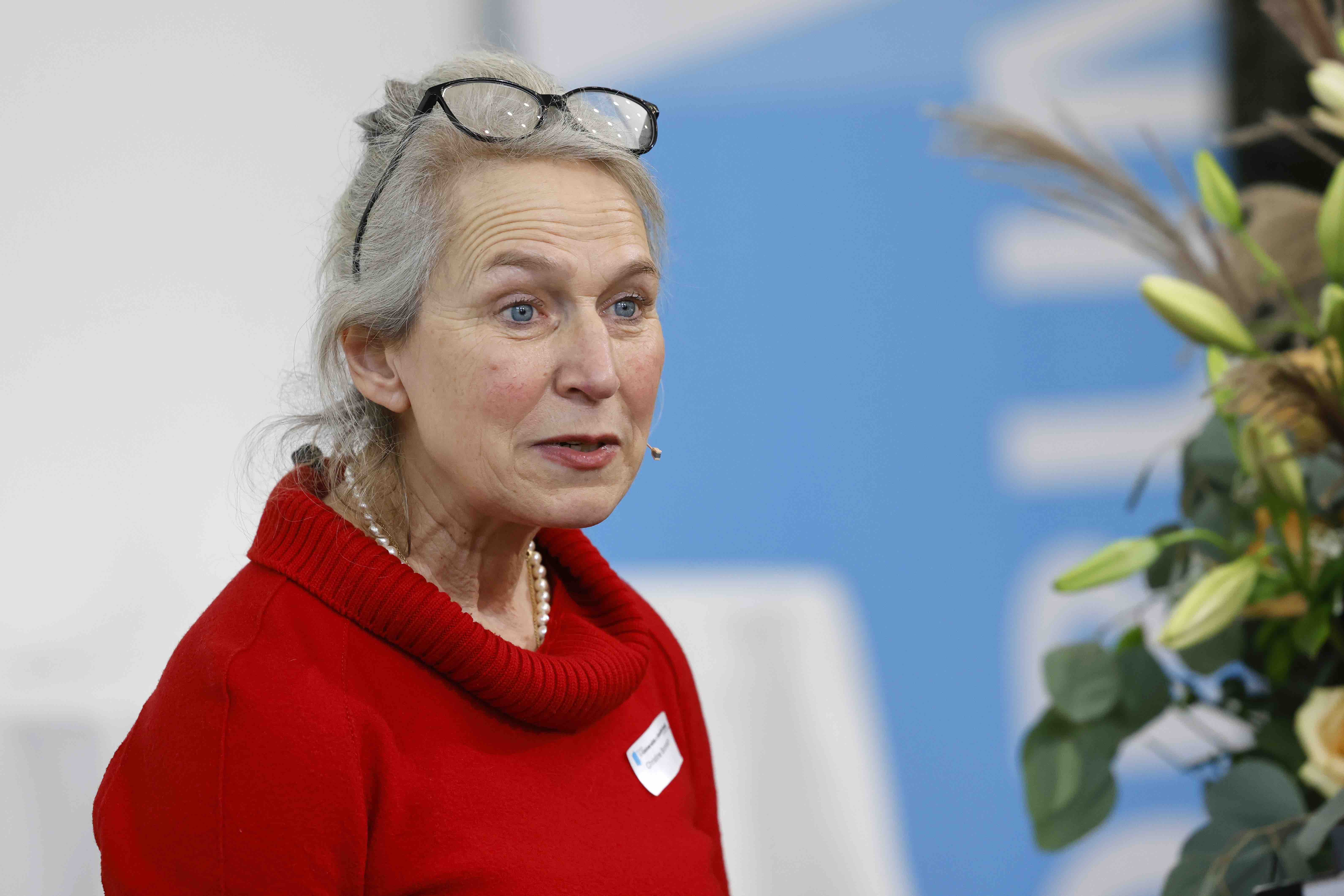 Porträtaufnahme der Referentin Prof. Dr. Christine Brombach. Sie trägt ein rotes Kleid. Im Hintergrund ist ein Banner mit dem blauweissen Forumslogo verschwommen zu sehen.